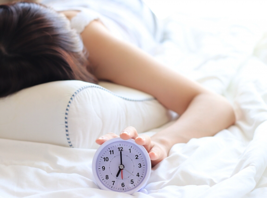 目覚し時計に手を伸ばす女性