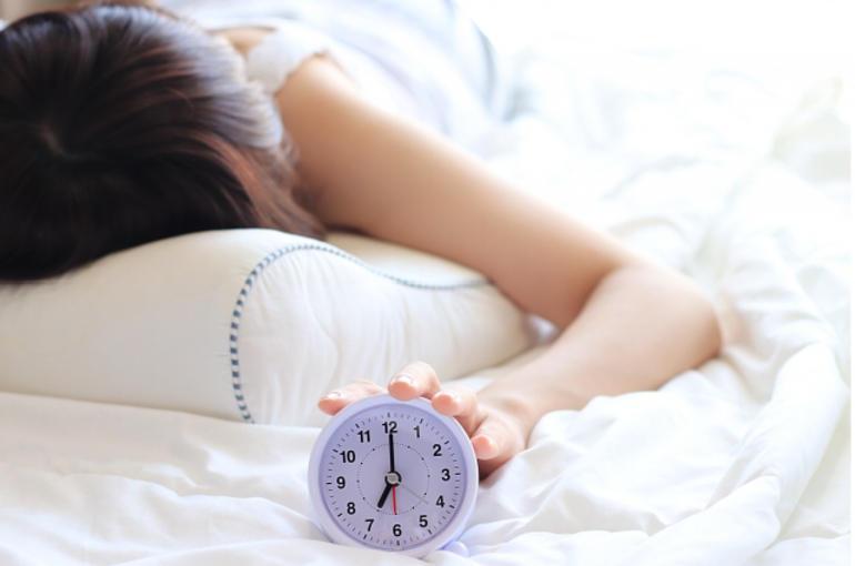 目覚し時計に手を伸ばす女性